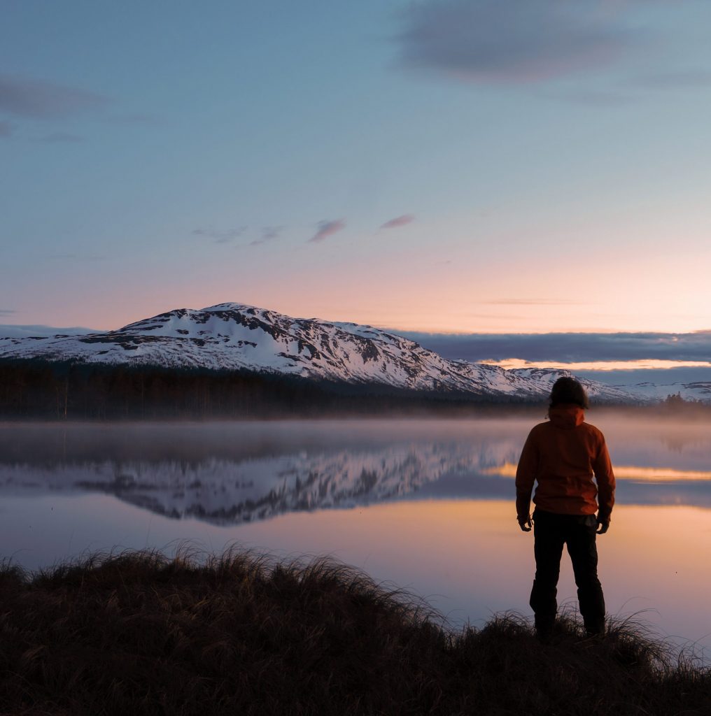 Un homme se tenant devant un paysage de mer au coucher du soleil.